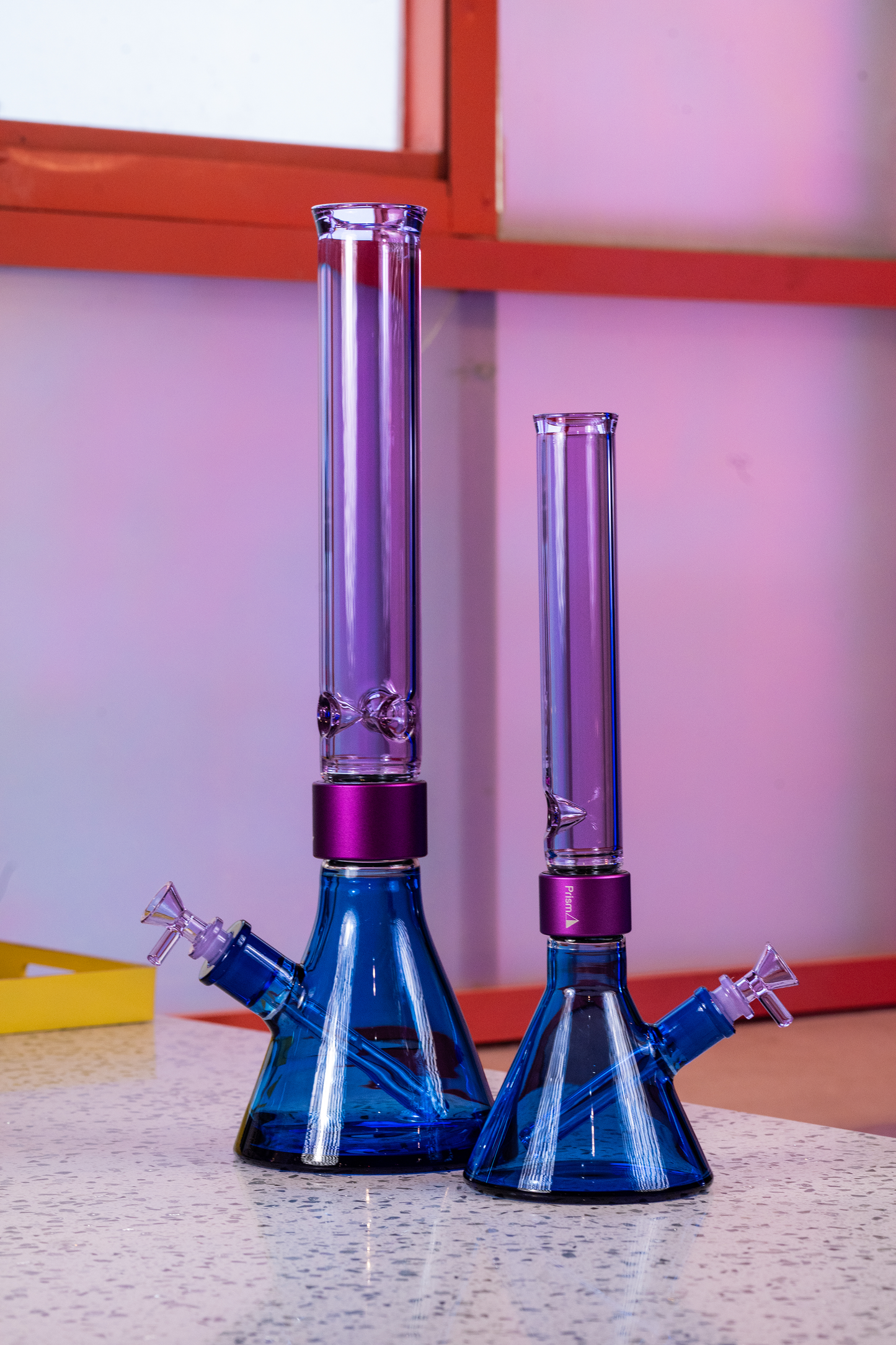 Two Prism modular beaker bongs from the Duo Collection standing side by side. On the left is a Classic Tall size and on the right is a MINI Tall size, both featuring a vibrant Sapphire Blue and Grape Jolly Rancher Purple color combination.