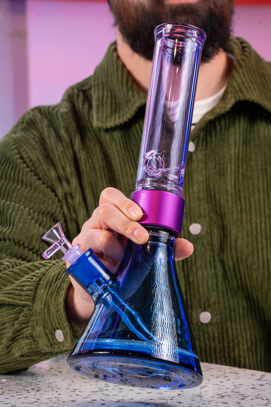 A man holding a Prism Water Pipes Duo Collection modular beaker bong in Sapphire Blue and Grape Jolly Rancher Purple glass. This custom glass pipe features a purple halo connector and illustrates the scale and assembly of the modular bong system.