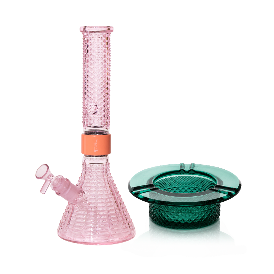 Jane West Ultimate Bundle featuring the pink Prism x Jane West MINI Beaker Bong and matching Twenties Collection Ashtray. The luxury smoking set highlights the diamond-patterned textured glassware and cohesive pink color. The MINI Beaker water pipe is shown with a coral-colored MINI halo connector and 14mm male bowl. Premium glass bundle, designer smoking set, collaborative cannabis glassware, matching amber bong and ashtray, Twenties Collection water pipe.