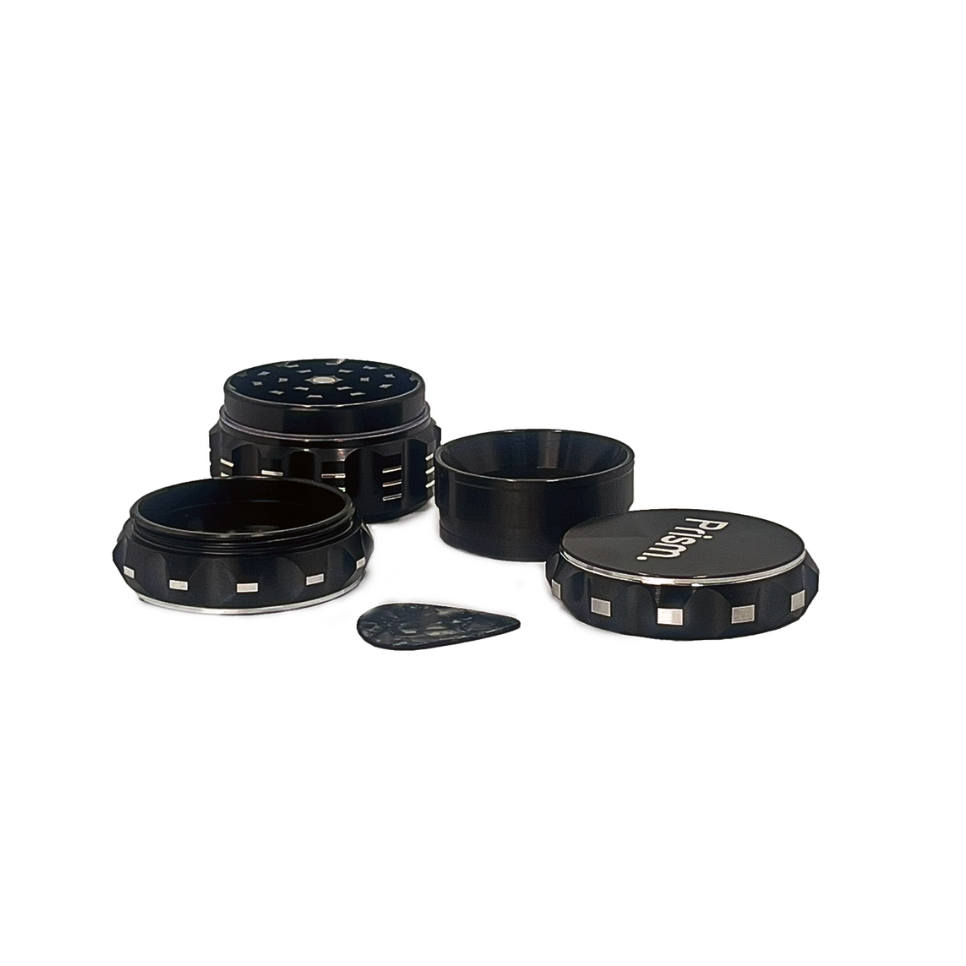 Prism Water Pipes black 3-piece herb grinder fully disassembled. Shows grinding teeth, herb chamber, kief screen, and KOZO guitar pick scraper.