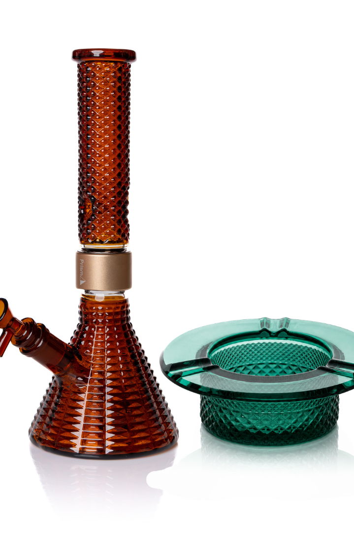 Jane West Ultimate Bundle featuring the amber Prism x Jane West MINI Beaker Bong and matching Twenties Collection Ashtray. The luxury smoking set highlights the diamond-patterned textured glassware and cohesive amber color. The MINI Beaker water pipe is shown with a gold-colored MINI halo connector and 14mm male bowl. Premium glass bundle, designer smoking set, collaborative cannabis glassware, matching amber bong and ashtray, Twenties Collection water pipe.