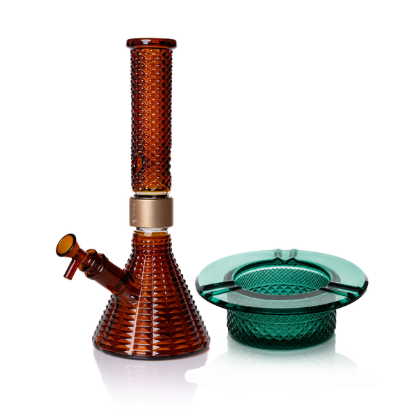 Jane West Ultimate Bundle featuring the amber Prism x Jane West MINI Beaker Bong and matching Twenties Collection Ashtray. The luxury smoking set highlights the diamond-patterned textured glassware and cohesive amber color. The MINI Beaker water pipe is shown with a gold-colored MINI halo connector and 14mm male bowl. Premium glass bundle, designer smoking set, collaborative cannabis glassware, matching amber bong and ashtray, Twenties Collection water pipe.